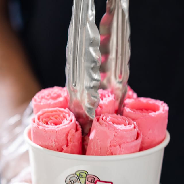 Pink strawberry ice cream rolls being served fresh in a cup